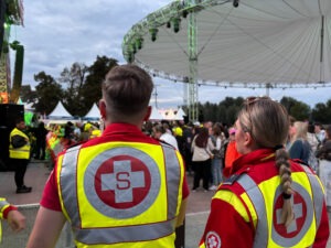 1 Samariterin und 1 Samariter in Uniform beobachten die Zuseher und die Bühne