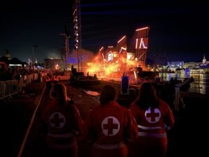 3 Sanitäterinnen blicken auf das rauchende, beleuchtete Schiff der Klangwolke 2025