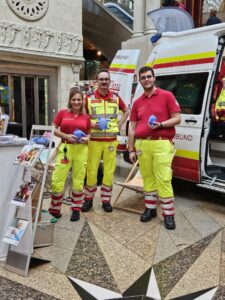 3 Sanitäter stehen auf einem Stand der Krone Gesund Tage vor einem Rettungsfahrzeug