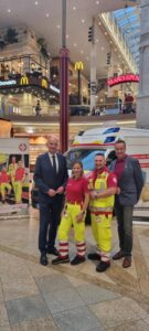 Zwei Sanitäter stehen mit LR Dörfel und Mag. Christian Wagner vor einem Rettungsfahrzeug des Samariterbundes