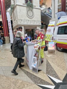 Sanitäter stehen auf einem Stand der Krone Gesund Tage vor einem Rettungsfahrzeug und sind im Gespräch mit Besucher:innen