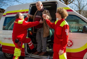 zwei Sanitäter helfen einem alten Mann aus dem Behindertenfahrzeug