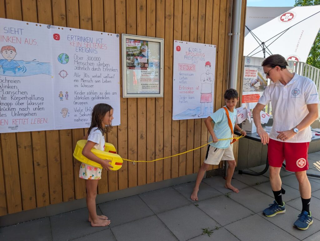 Am Pichlingersee üben Kinder mit Wasserrettung und Rettungsboje den sicheren Umgang mit dem gelben Schwimmgurt.